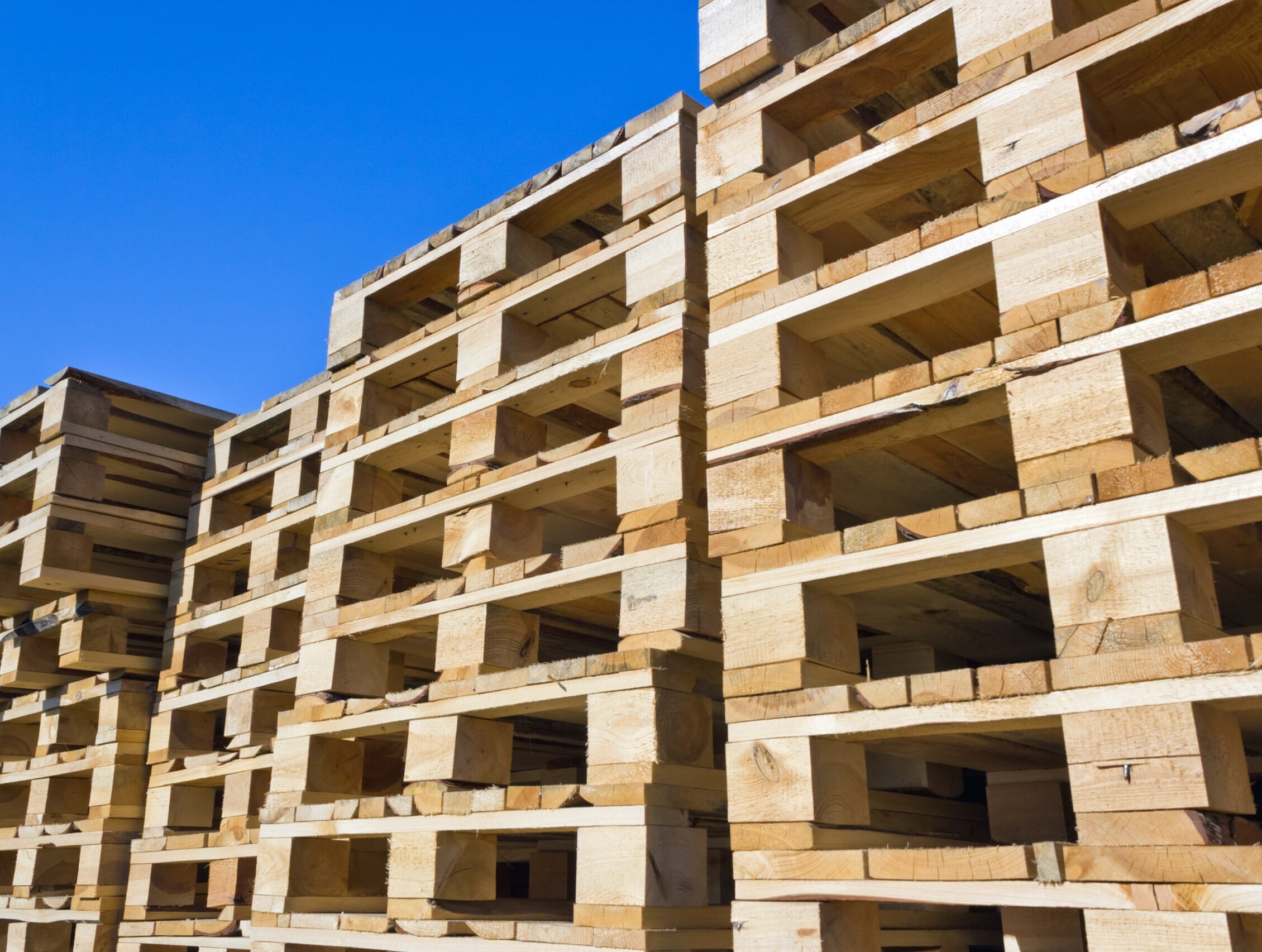 Stacked timber pallets outdoors against a blue sky — Australian standard wooden pallets for warehousing and distribution