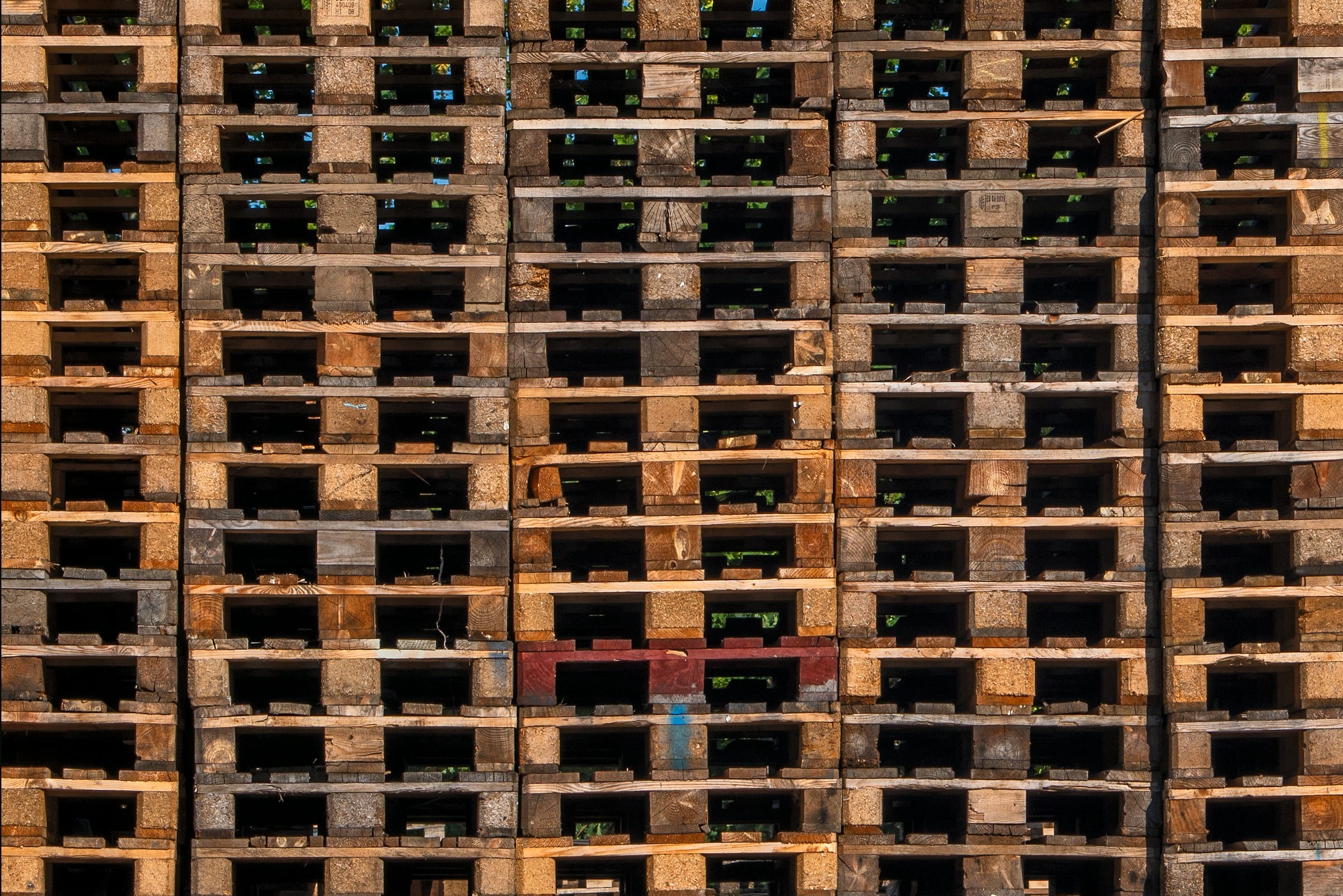 A large stack of wooden pallets arranged in neat rows, showing variations in texture and color, symbolizing storage and logistics efficiency for businesses. Perfect visual for the article “How to Choose the Right Pallet for Your Business.