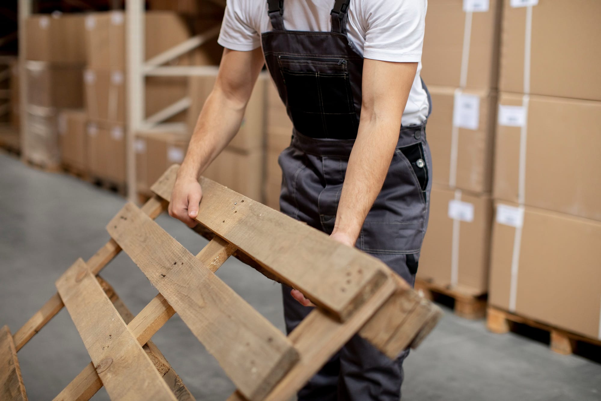 Warehouse worker lifting a wooden pallet, showing the importance of pallet use in logistics and storage across multiple sectors in Why Pallets Matter in Every Industry.