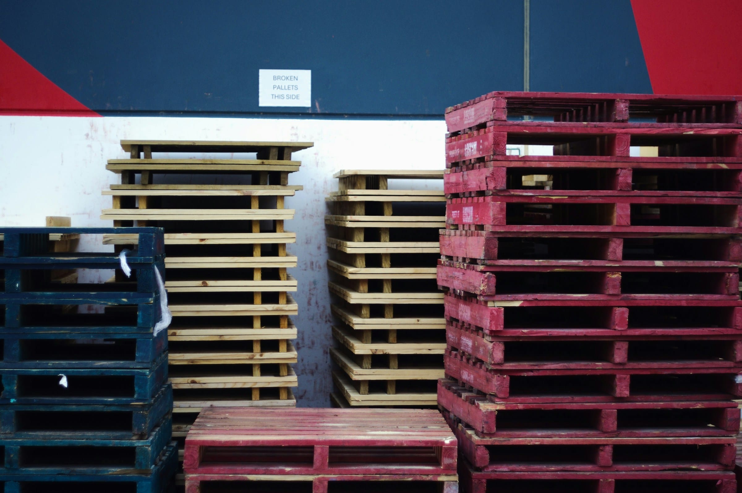 Stacks of colored wooden pallets in a warehouse, showing different pallet types used when choosing to buy or rent pallets for business logistics