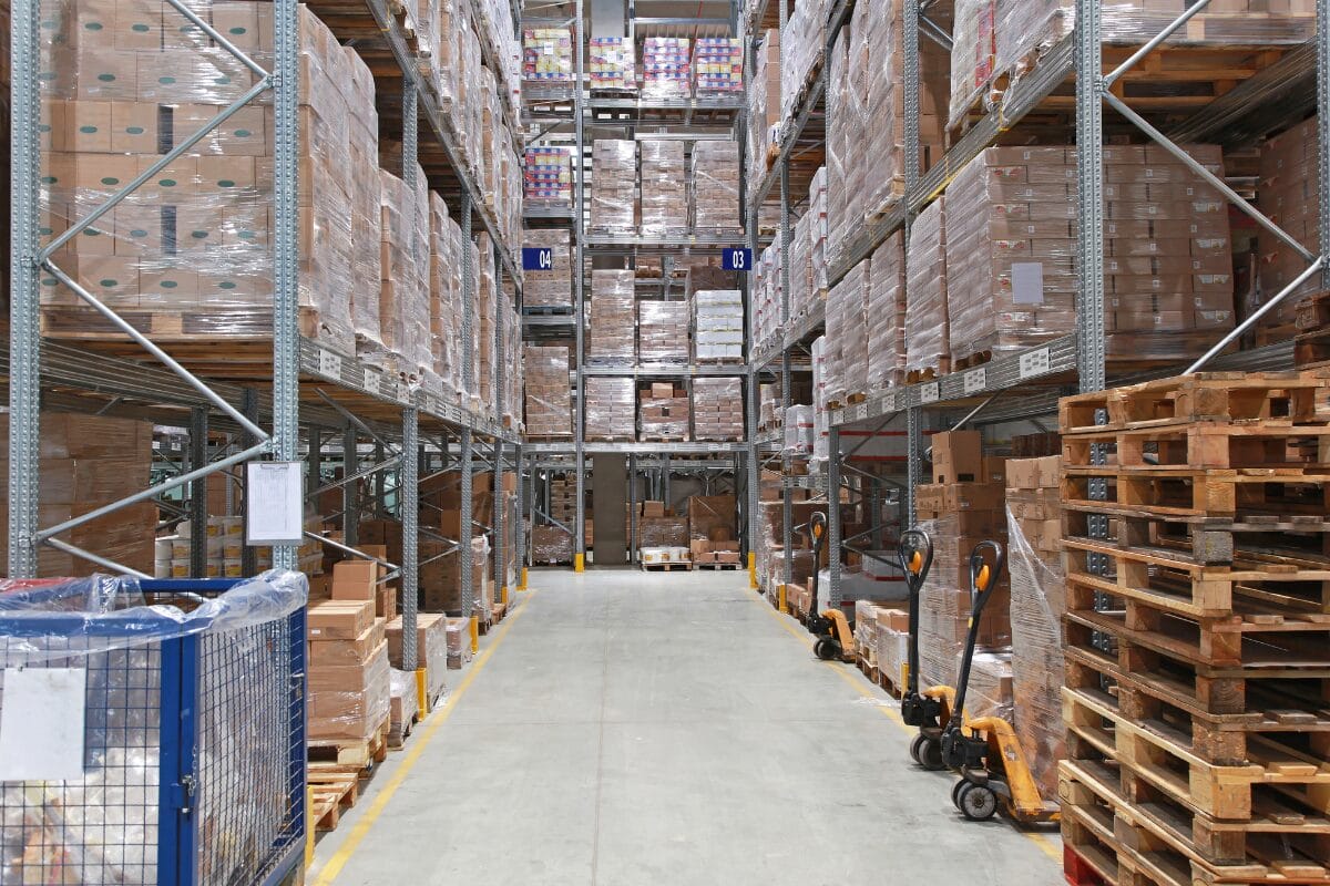 Large warehouse aisle with pallet racking filled with shrink-wrapped goods on wooden pallets