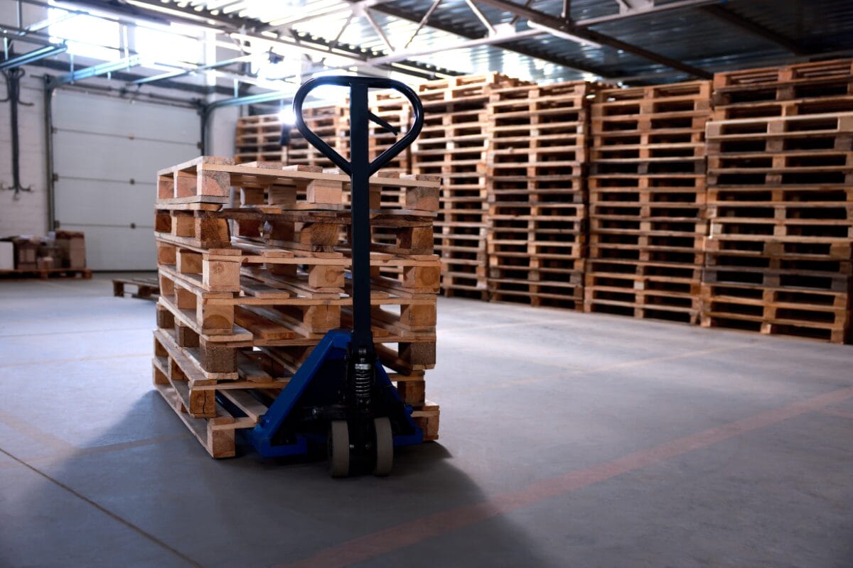 Manual pallet jack positioned beside stacked pallets in a warehouse facility