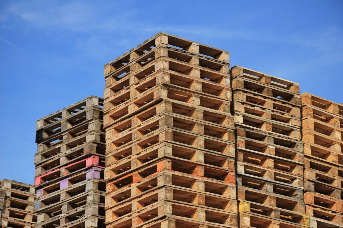 Stacked wooden pallets stored outdoors against a blue sky