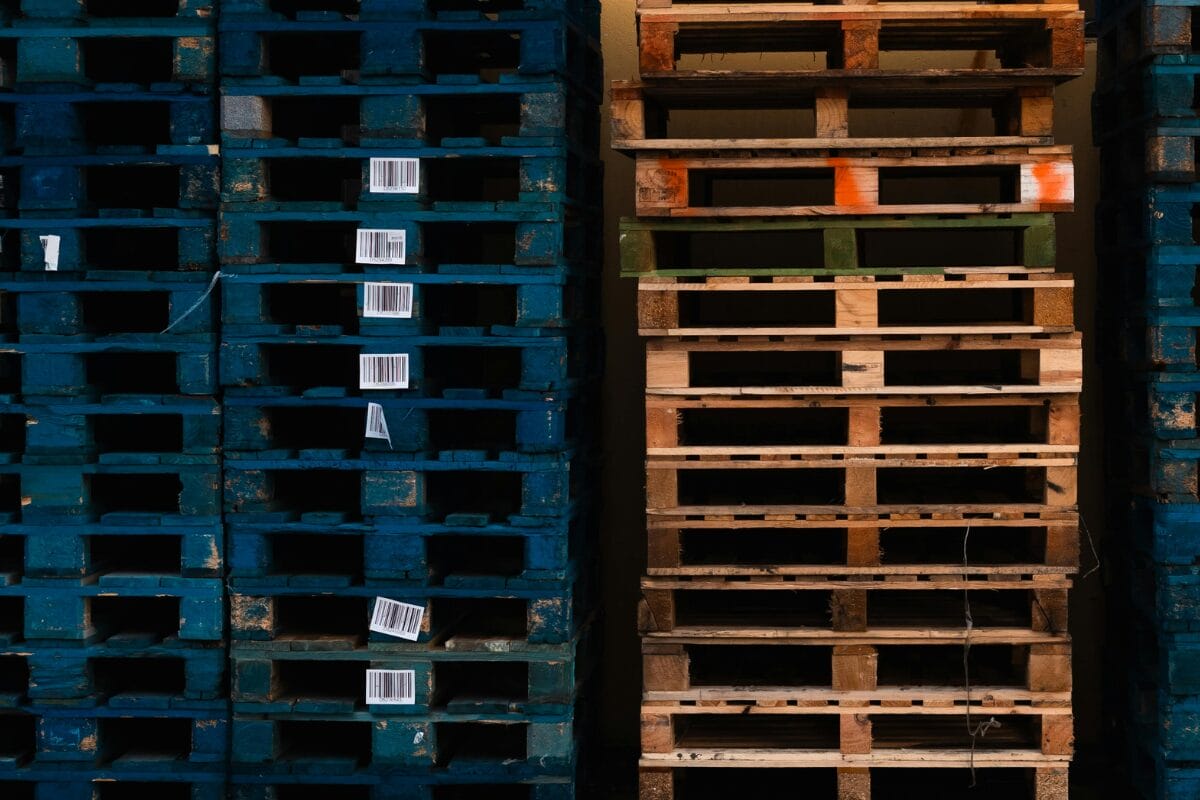 Stacked wooden pallets with painted markings and barcodes in a storage area