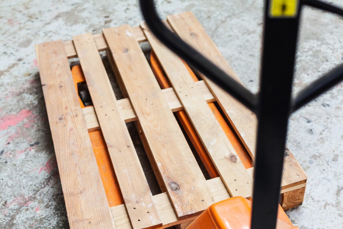 Wooden pallet on a pallet jack with visible forklift entry gaps and deck boards